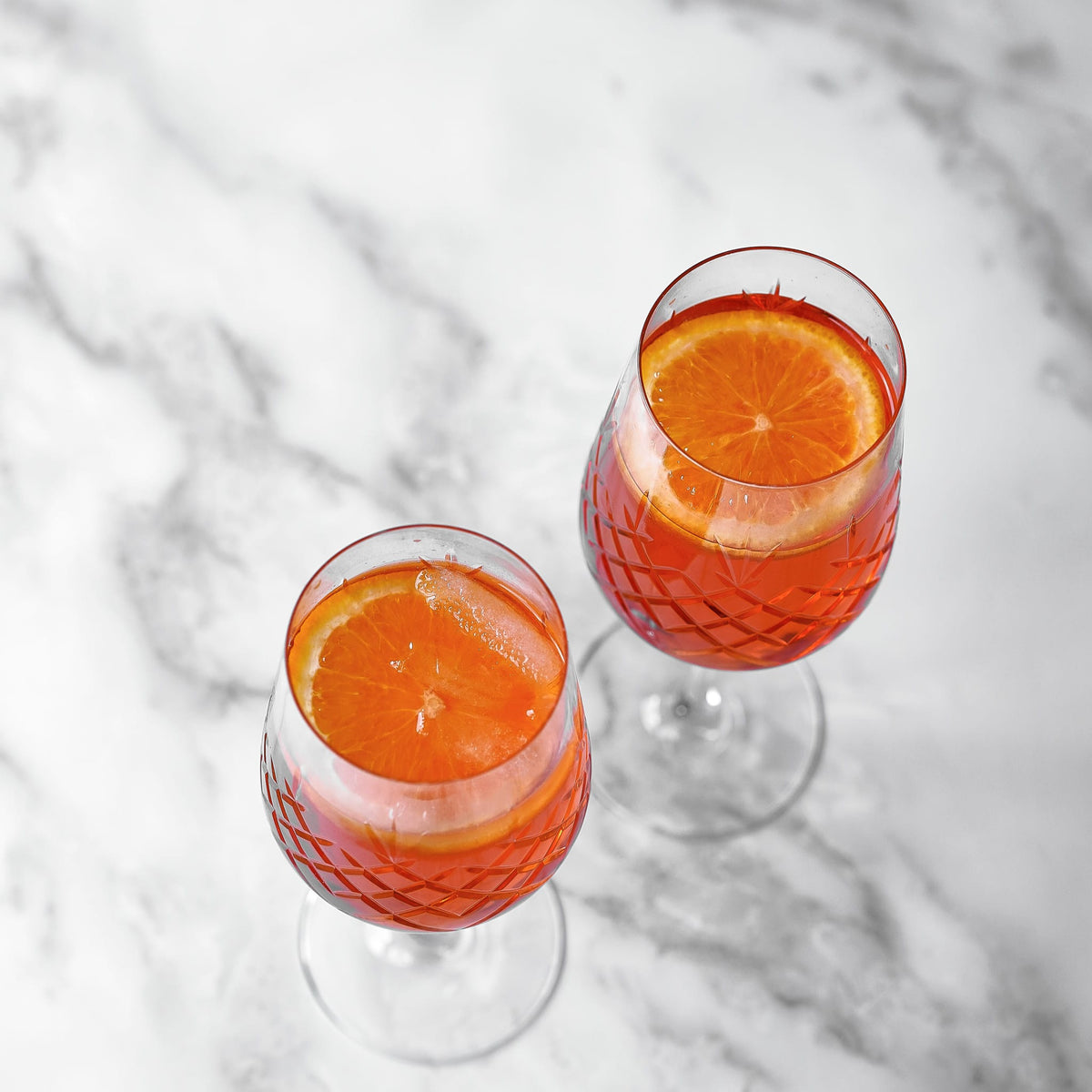 To klart facetslebne rødvinsglas med riflet diamantmønster fra Frederik Bagger, fyldt med orange drink