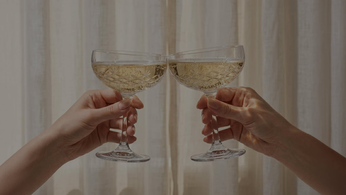 To hænder skåler med champagneglas fyldt med lys drik foran gardiner